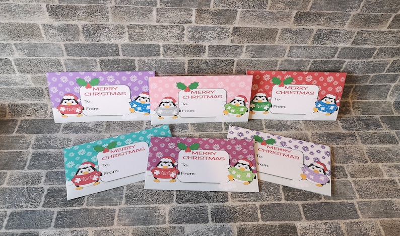 May include: Six colorful gift tags featuring a penguin wearing a sweater and a Santa hat. Each tag has a snowflake pattern and says "Merry Christmas" with space to write "To" and "From".