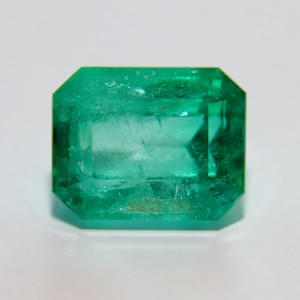 Puede incluir: Una gema de esmeralda verde vibrante con un corte facetado. La esmeralda tiene una forma rectangular con un borde ligeramente redondeado.