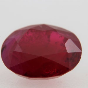 May include: A deep red oval-shaped gemstone with a faceted cut.
