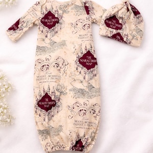 May include: A cream-colored baby gown and matching hat set. The set is printed with a map design and the words "The Marauders Map". The gown has long sleeves and a footed design. The hat is a knotted style.