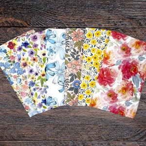 May include: Five different floral patterned fabric swatches. The swatches are arranged in a fan shape with the top of each swatch facing the viewer. The swatches feature a variety of floral patterns in shades of blue, pink, yellow, and red.
