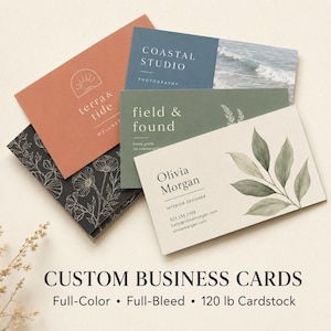 May include: A collection of rectangular business cards featuring various designs including a terracotta card with a sun icon, a blue card with ocean imagery, a black card with white floral line art, a green card, and a cream card with green leaves.