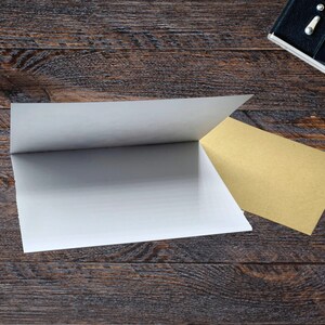 Puede incluir: Una tarjeta blanca plegada y una tarjeta beige est&aacute;n sobre una superficie de madera oscura. Una c&aacute;mara vintage y unas gafas est&aacute;n en el fondo. Las tarjetas est&aacute;n dispuestas para crear una exhibici&oacute;n visual.