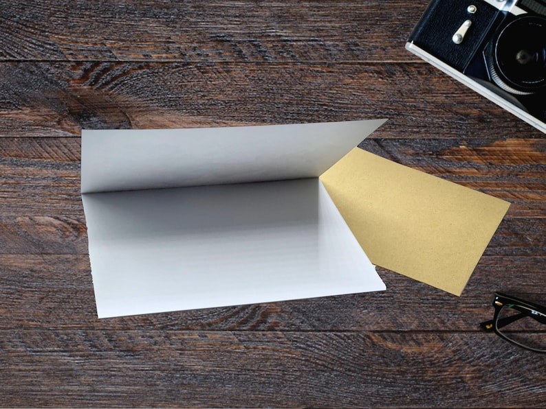 Puede incluir: Una tarjeta blanca plegada y una tarjeta beige est&aacute;n sobre una superficie de madera oscura. Una c&aacute;mara vintage y unas gafas est&aacute;n en el fondo. Las tarjetas est&aacute;n dispuestas para crear una exhibici&oacute;n visual.