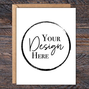 Puede incluir: Una tarjeta de felicitaci&oacute;n en blanco con un sobre de papel kraft. La tarjeta blanca presenta un dise&ntilde;o circular negro con las palabras "Your Design Here" en un estilo manuscrito. El fondo es una superficie de madera oscura.