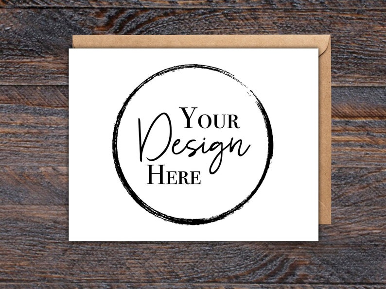 Puede incluir: Una tarjeta blanca con el texto "YOUR Design HERE" dentro de un c&iacute;rculo negro, colocada en un sobre de papel kraft marr&oacute;n. El fondo es una veta de madera oscura.
