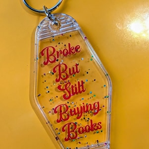 May include: A white ceramic mug with a black handle and the text "But First, Coffee" in a bold, black font. The mug is set against a blurred background, suggesting a cozy setting.