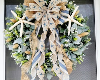 May include: A wreath made of green and gray foliage with two white starfish and a blue and white ribbon with a burlap bow. The ribbon has a star pattern.