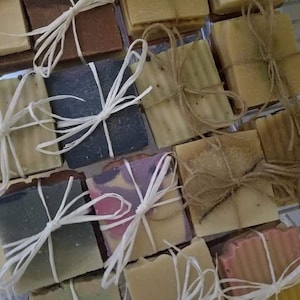 May include: A collection of handmade soap bars wrapped in twine and tied with white ribbon. The soap bars are various colors and patterns.