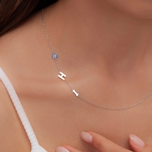 Può includere: Una collana a catena d'argento con un ciondolo di occhio blu malvagio e le lettere 'HI' che pendono.