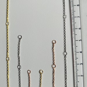 Puede incluir: Cinco extensores de cadena diferentes en oro, plata y oro rosa. Las cadenas miden aproximadamente 10 cm de largo y tienen un cierre de langosta en el extremo.