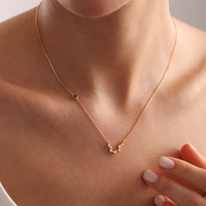 May include: A gold chain necklace with a small red gemstone and a constellation design with small clear gemstones.