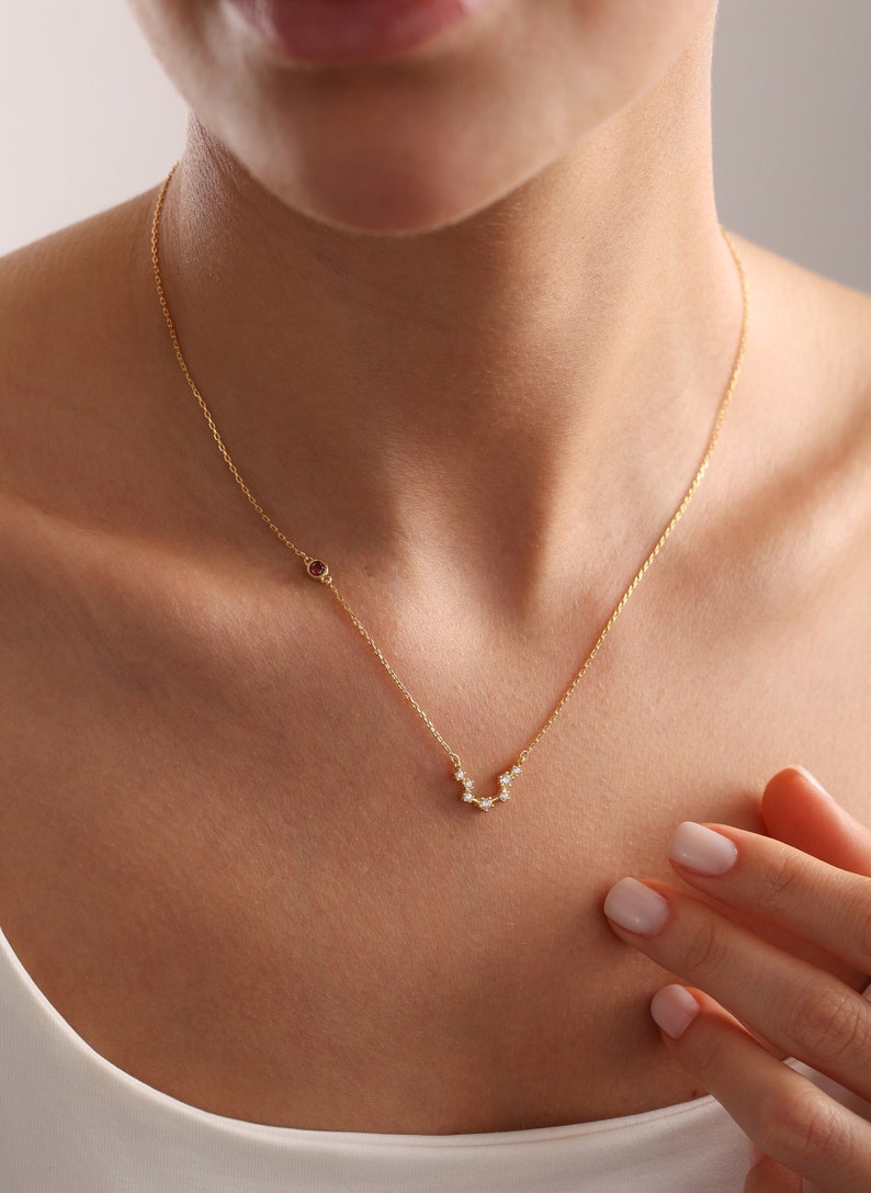 May include: A gold chain necklace with a small red gemstone and a constellation design with small clear gemstones.