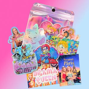 Pu&ograve; includere: Una collezione di adesivi olografici con personaggi dei cartoni animati e riferimenti alla cultura pop. I disegni includono personaggi di "The Powerpuff Girls", "Sabrina, vita da strega" e "Passport to Paris". Gli adesivi sono confezionati in un sacchetto trasparente e iridescente.