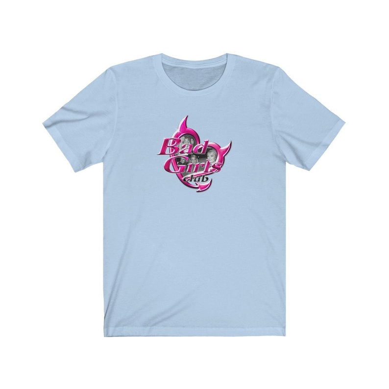 May include: Pale blue t-shirt with a pink and silver graphic. The graphic says "Bad Girls Club" and features images of three women. The text is in a decorative font. The shirt is made of a soft material.