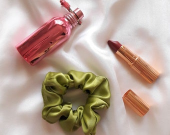 May include: A green satin scrunchie, a pink glass bottle of perfume, and a red lipstick with a gold tube.