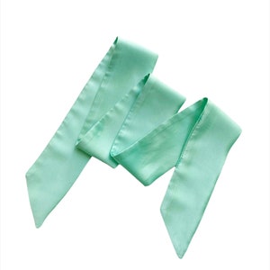 May include: A light green satin ribbon, tied in a loose knot, ready for wrapping gifts or adding a touch of elegance to hair.