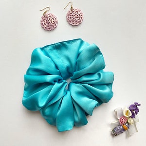 May include: A turquoise blue satin scrunchie with two pink floral earrings.