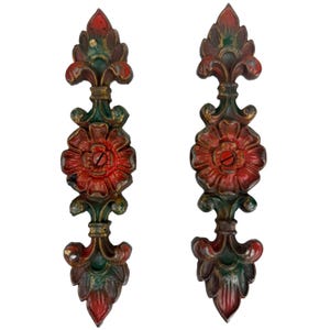 May include: Two ornate, vintage metal decorative pieces. Each piece features a red flower, green leaves, and gold accents. The pieces are vertically oriented and appear to be part of a larger decorative element.