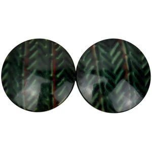 Puede incluir: Dos botones redondos de cerámica con un patrón geométrico verde y rojo.