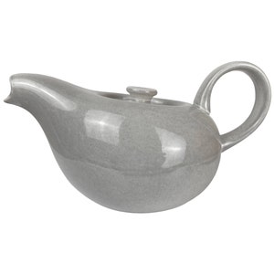 Könnte beinhalten: Eine graue Teekanne aus Keramik mit einem abgerundeten Körper und einem geschwungenen Ausguss. Die Teekanne hat einen einzigen Henkel und einen kleinen Knopf auf dem Deckel.