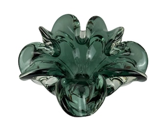 May include: A green glass ashtray with a flower-like design. The ashtray is made of thick glass and has a smooth, rounded surface.