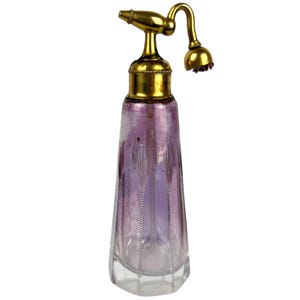 May include: A vintage glass perfume bottle with a gold metal atomizer and a clear glass stopper. The bottle is decorated with a geometric pattern and has a pale purple hue.