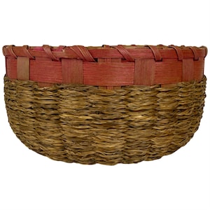May include: A round basket featuring a lower section made of woven brown natural fibres and an upper rim constructed from flat, reddish-brown wooden splints woven in a horizontal pattern with a braided edge along the top opening.