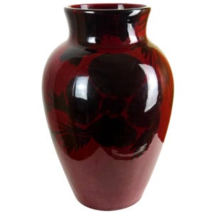 May include: A glossy, bulbous ceramic vase featuring a deep burgundy red base color with dark, almost black, floral patterns painted across the surface. The vase has a wide, rounded body that tapers toward a smooth, open circular rim at the top.