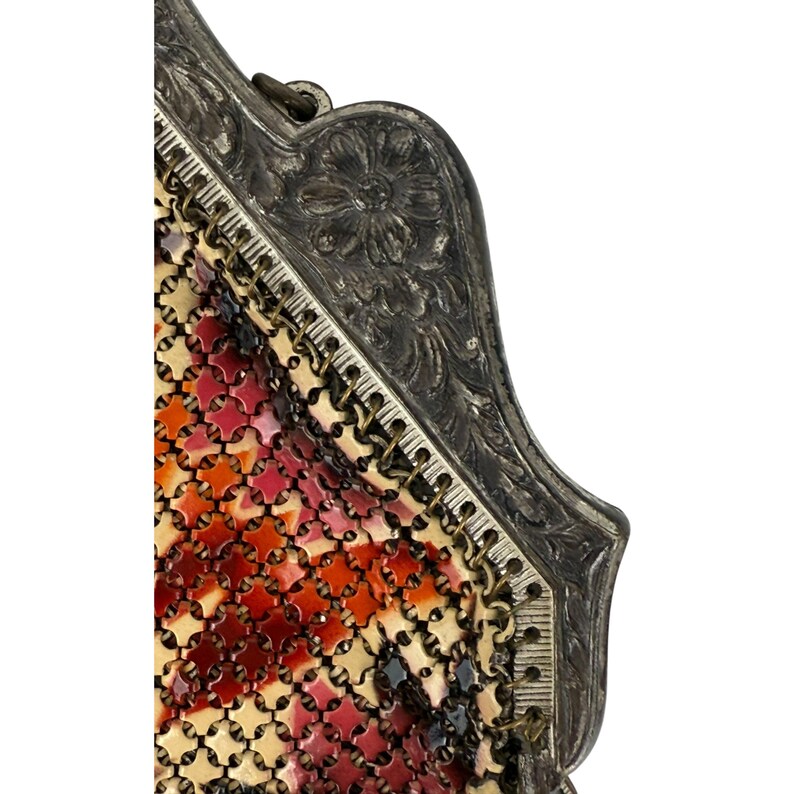 May include: Close-up of a vintage silver mesh purse with a floral design on the frame. The mesh is made of small, red, orange, and white squares.