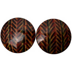 May include: A pair of round, brown earrings with a black and green geometric pattern.