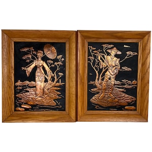 May include: Two framed copper relief wall hangings with a black background. The left panel depicts a woman in a traditional Japanese dress holding an umbrella. The right panel depicts a man in a traditional Japanese outfit playing a musical instrument.