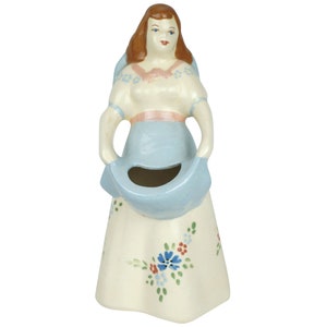 May include: A ceramic figurine of a woman in a blue and white dress holding a blue planter. The planter has a floral design and is ideal for small plants.