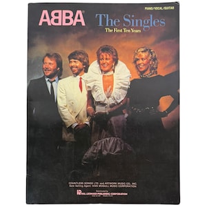 Könnte beinhalten: Ein Musiknotenbuch mit dem Titel ABBA The Singles The First Ten Years, das ein Foto der vier Bandmitglieder zeigt. Das Cover zeigt die Gruppe in formeller Kleidung vor einem Sonnenuntergangshintergrund mit Hinweisen für Klavier, Gesang und Gitarre.