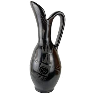 May include: Black ceramic pitcher with a geometric design. The pitcher has a wide mouth and a handle.