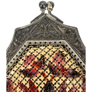 May include: A vintage silver and gold mesh purse with a floral design. The purse has a hinged top with a decorative clasp.