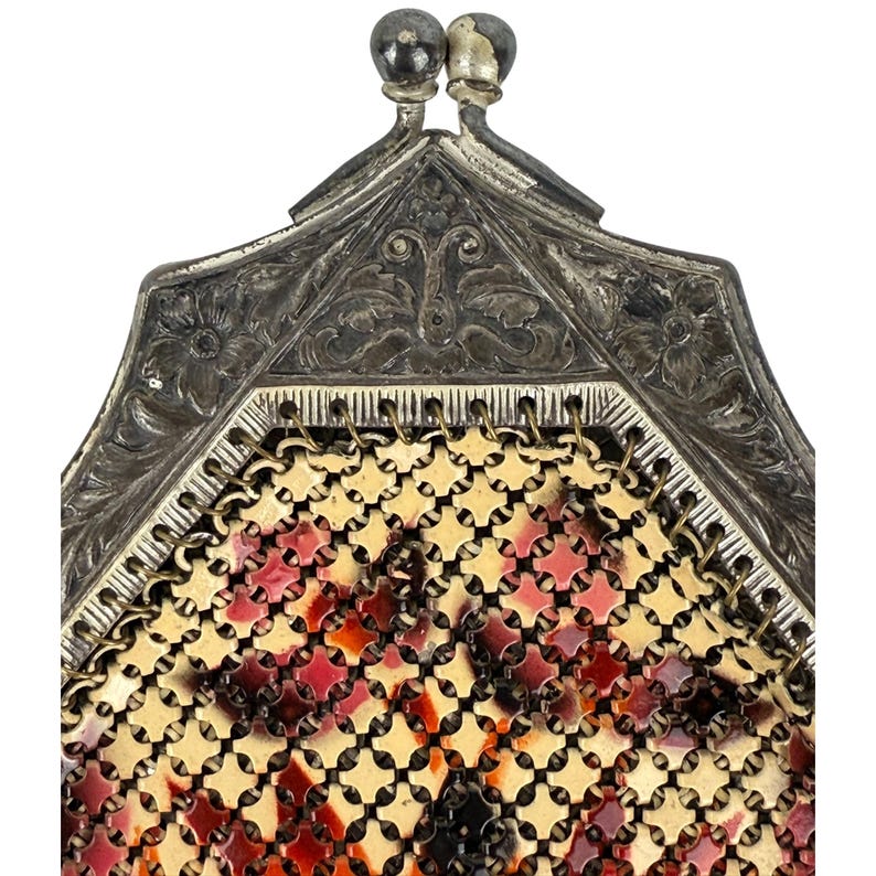 May include: A vintage silver and gold mesh purse with a floral design. The purse has a hinged top with a decorative clasp.
