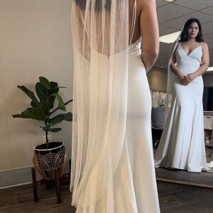 May include: A white wedding dress with a long train and a white veil. The dress has a simple, elegant design and is made of a smooth fabric.