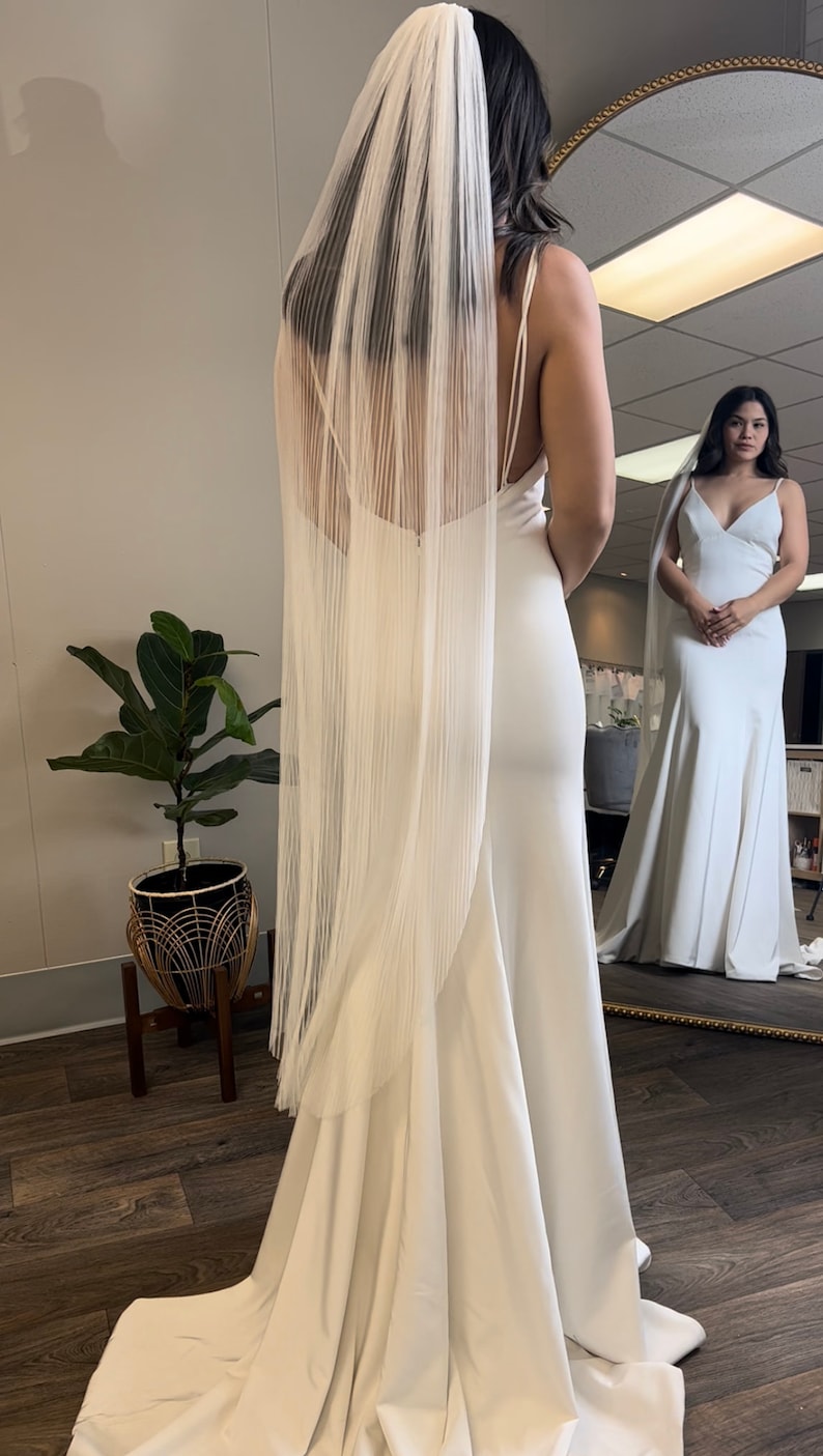 May include: A white wedding dress with a long train and a white veil. The dress has a simple, elegant design and is made of a smooth fabric.