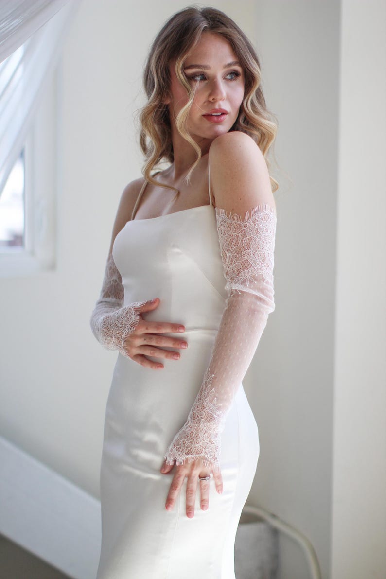 May include: A white strapless dress with delicate lace sleeves. The dress has a fitted bodice and a flowing skirt.