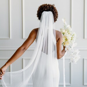 May include: A bride wearing a white wedding dress and a long, white veil. She is holding a bouquet of white flowers.