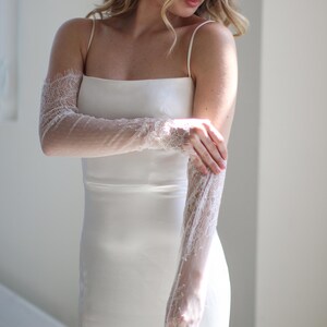 May include: A white satin dress with delicate lace sleeves. The sleeves are sheer and have a floral pattern. The dress is sleeveless and has a simple, elegant design.