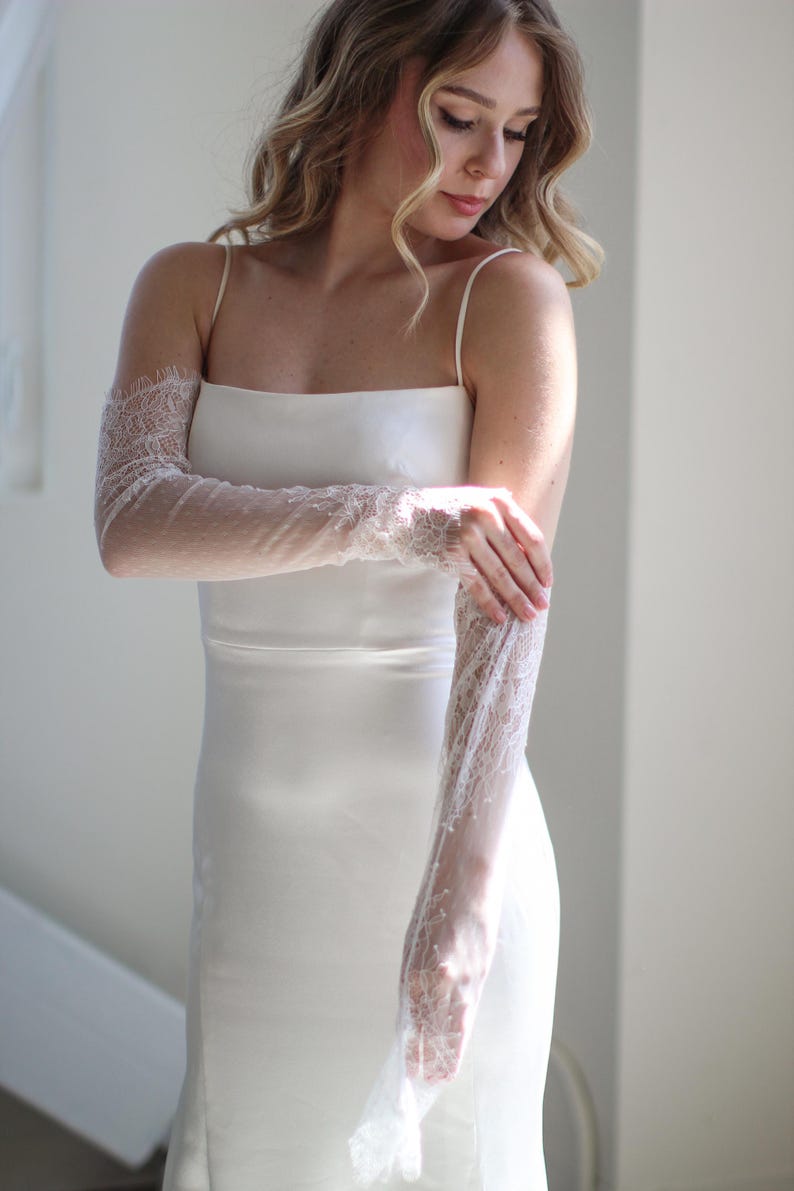 May include: A white satin dress with delicate lace sleeves. The sleeves are sheer and have a floral pattern. The dress is sleeveless and has a simple, elegant design.
