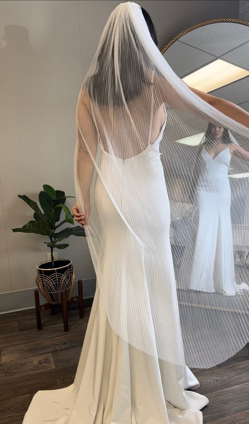 May include: A white wedding veil with a pleated design. The veil is draped over a white wedding dress.