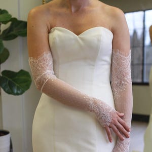 May include: A white strapless wedding dress with delicate lace gloves. The gloves are sheer and have a floral pattern.