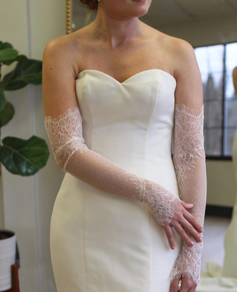 May include: A white strapless wedding dress with delicate lace gloves. The gloves are sheer and have a floral pattern.
