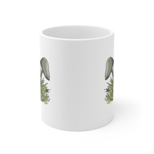 Pode incluir: Caneca de cer&acirc;mica branca com uma ilustra&ccedil;&atilde;o de cogumelo verde e cinza de cada lado.