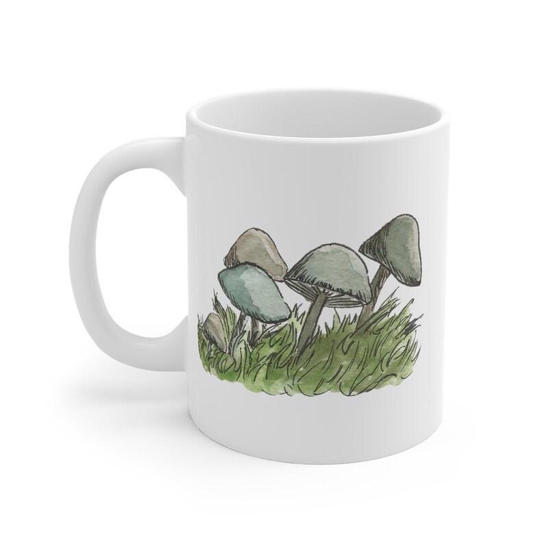 Pode incluir: Caneca de cer&acirc;mica branca com uma ilustra&ccedil;&atilde;o em aquarela de cogumelos em grama verde.