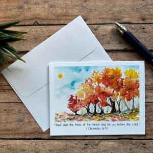 May include: Watercolor greeting card featuring a landscape of autumn trees in shades of red, orange, and yellow under a blue sky with a yellow sun. The card includes the text "Then shall the trees of the forest sing for joy before the Lord." I Chronicles 16:33.