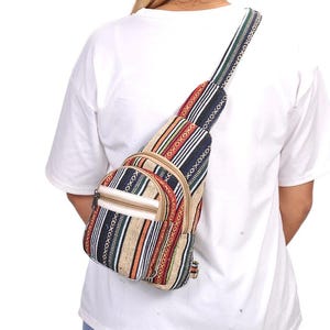 May include: A crossbody sling bag featuring a woven fabric with a multi-colored striped pattern in shades of black, white, orange, and tan. The bag includes a front zippered pocket, a main compartment, and an adjustable shoulder strap.